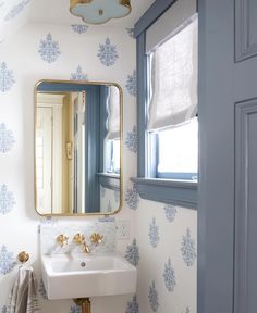 a bathroom with blue and white wallpaper on the walls, and a mirror above it