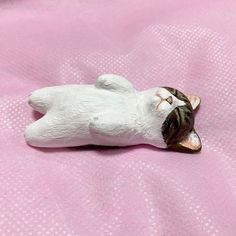 a small cat figurine laying on top of a pink blanket with its eyes closed