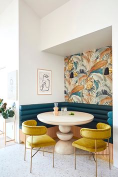 a white table with four yellow chairs in front of a colorful wallpapered area