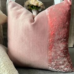 a pink pillow sitting on top of a couch next to a vase with flowers in it