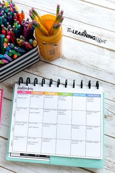 an open planner with pencils and markers on it next to a cup full of colored crayons