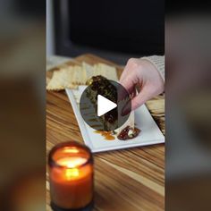 a person is eating food on a plate with a candle in the foreground and a television screen behind them