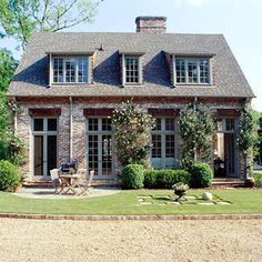 a large brick house with lots of windows and plants on the front lawn in front of it