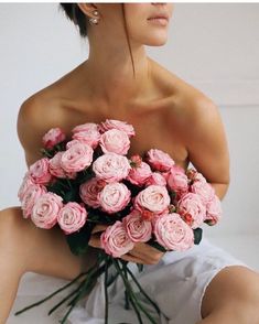 a woman sitting on the floor holding a bouquet of pink roses