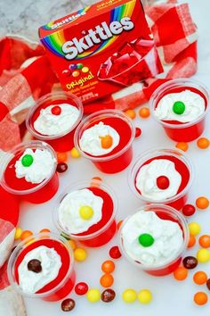 small red cups filled with white frosting and candy candies next to a box of skittles