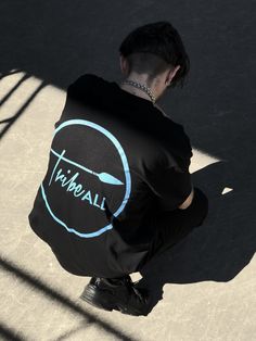 a man sitting on the ground with his back turned to the camera, wearing a black t - shirt that says tryball