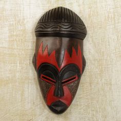 a wooden mask hanging on the wall with red and black paint painted on it's face