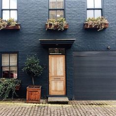 a blue building with potted plants on the front and side windows, along with a wooden door