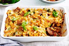 a casserole dish filled with pasta, sausage and spinach on a table