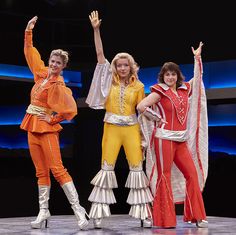 three women in colorful outfits on stage with one holding her arms up to the side