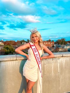 a beautiful woman in a white dress posing for a photo with a crown on her head