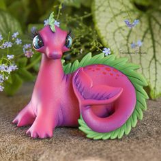 a pink toy sitting on top of a rock next to some flowers and green leaves