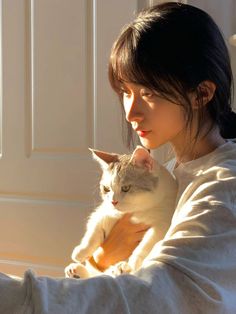 a woman holding a cat in her arms while sitting on the floor next to a door