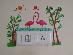 two pink flamingos standing on top of a white light switch box with trees and birds painted on it