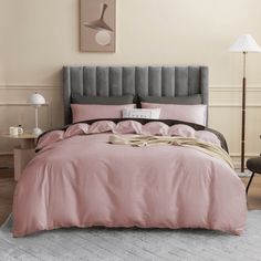 a bed with pink sheets and pillows on top of it in a room next to a chair