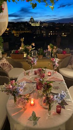 the table is set with flowers, candles and plates in front of a cityscape