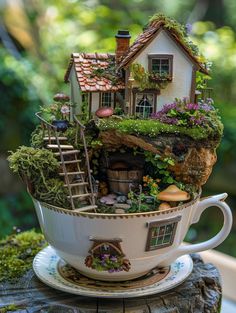 a teacup filled with plants and houses on top of a tree stump in the woods