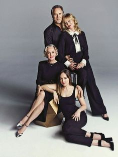 three women and one man are posing for a photo together in front of a gray background