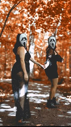 two women in masks are holding hands with each other outside on a sunny day, surrounded by trees and leaves