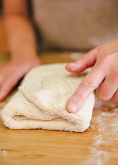 a person kneading dough on top of a wooden table