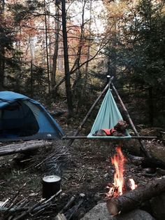 two tents set up in the woods next to a campfire