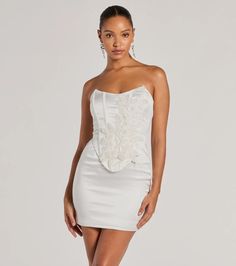 Chic with a stunning allure, the Hannah pearl beaded floral satin corset mini dress is an iconic choice for homecoming or your next formal party. Crafted with sleek satin woven fabric with a knit lining, she showcases a gorgeous embroidered floral applique accented with mini faux pearls, sequins, and beaded embellishments in an intricately placed design. The short dress features a strapless square neckline, a fitted corset bodice overlay with flexible boning to provide structure, a bold open lac Satin Mini Dress With Boned Bodice, Satin Mini Dress With Boned And Fitted Bodice, Satin Mini Corset Dress With Boned Bodice, Satin Boned Bodice Mini Corset Dress, Elegant Satin Mini Corset Dress, Satin Mini Dress With Boned Bodice For Prom, Elegant Mini Satin Corset Dress, Satin Corset Dress For Cocktail And Prom, Satin Corset Dress For Cocktail Prom Season