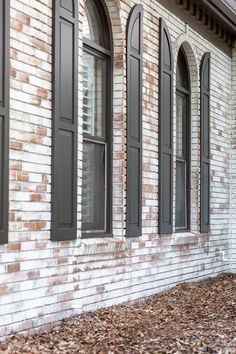 a brick building with three windows and some leaves on the ground