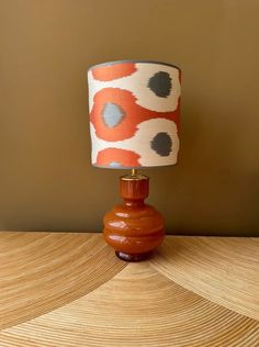 an orange and white lamp sitting on top of a wooden table next to a brown wall