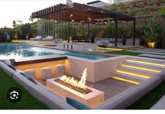 an outdoor fire pit in the middle of a lawn with lounge chairs and lights around it