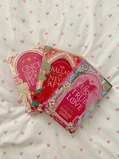 three books laying on top of a white bed covered in pink heart shaped sheets and pillows