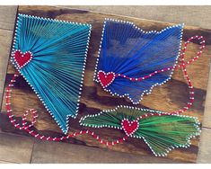 two blue and green string art pieces sitting on top of a wooden table