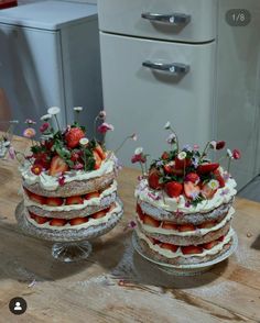 two cakes with strawberries and flowers on them sitting on a table next to an oven