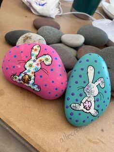 three painted rocks sitting next to each other on top of a wooden table covered in stones