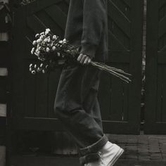 black and white photograph of person holding flowers in front of gated area with wooden door