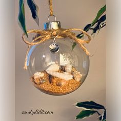 a glass ornament hanging from a rope with sea shells and sand in it