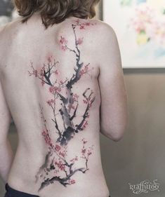 the back of a woman's body with flowers painted on it and branches in bloom