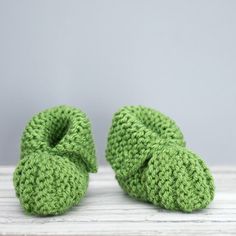 two crocheted green shoes sitting on top of a wooden table