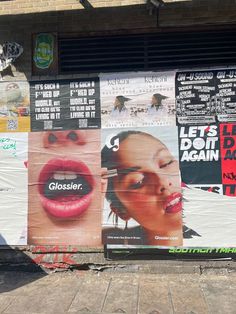 posters on the side of a building with woman's face painted on them and other advertisements