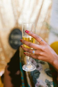 a woman's hand holding a wine glass in front of her face and wearing rings