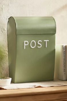 a green post box sitting on top of a table next to a cup and book