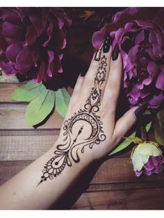 a woman's hand with a henna on it and purple flowers in the background