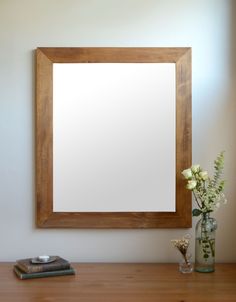 a wooden framed mirror sitting on top of a table next to a vase with flowers