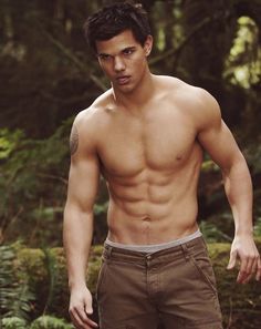 a shirtless man standing in the woods with his hands on his hips and looking at the camera