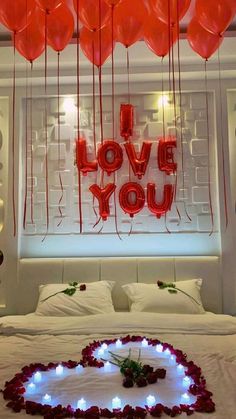 a bed with red balloons floating in the air above it and a heart shaped pillow