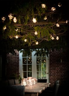 a dining room table with candles and lights hanging from the branches over it, in front of a window