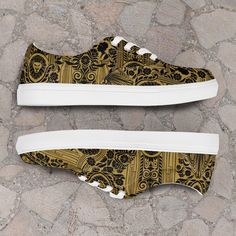 a pair of shoes with gold and black designs on the side, sitting on cobblestone