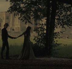 a man and woman holding hands in front of a tree