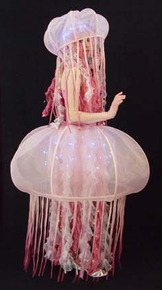 a mannequin dressed as a jellyfish with pink hair and white dress, standing in front of a black background