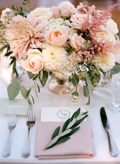 a vase filled with lots of flowers on top of a white table covered in silverware