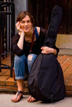 a woman sitting on the ground next to a guitar case